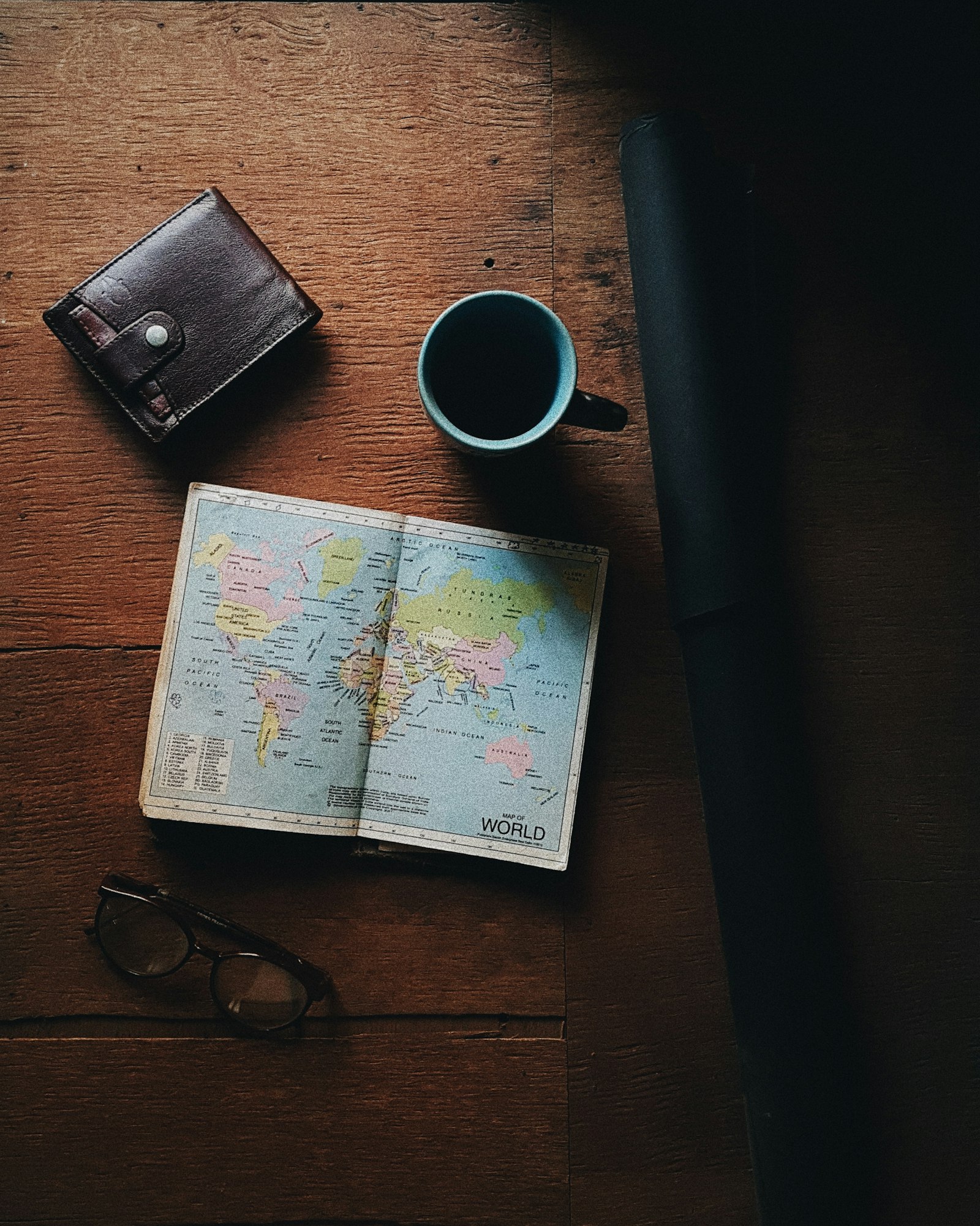 An open notebook, a folded map, and coffee on a wooden table